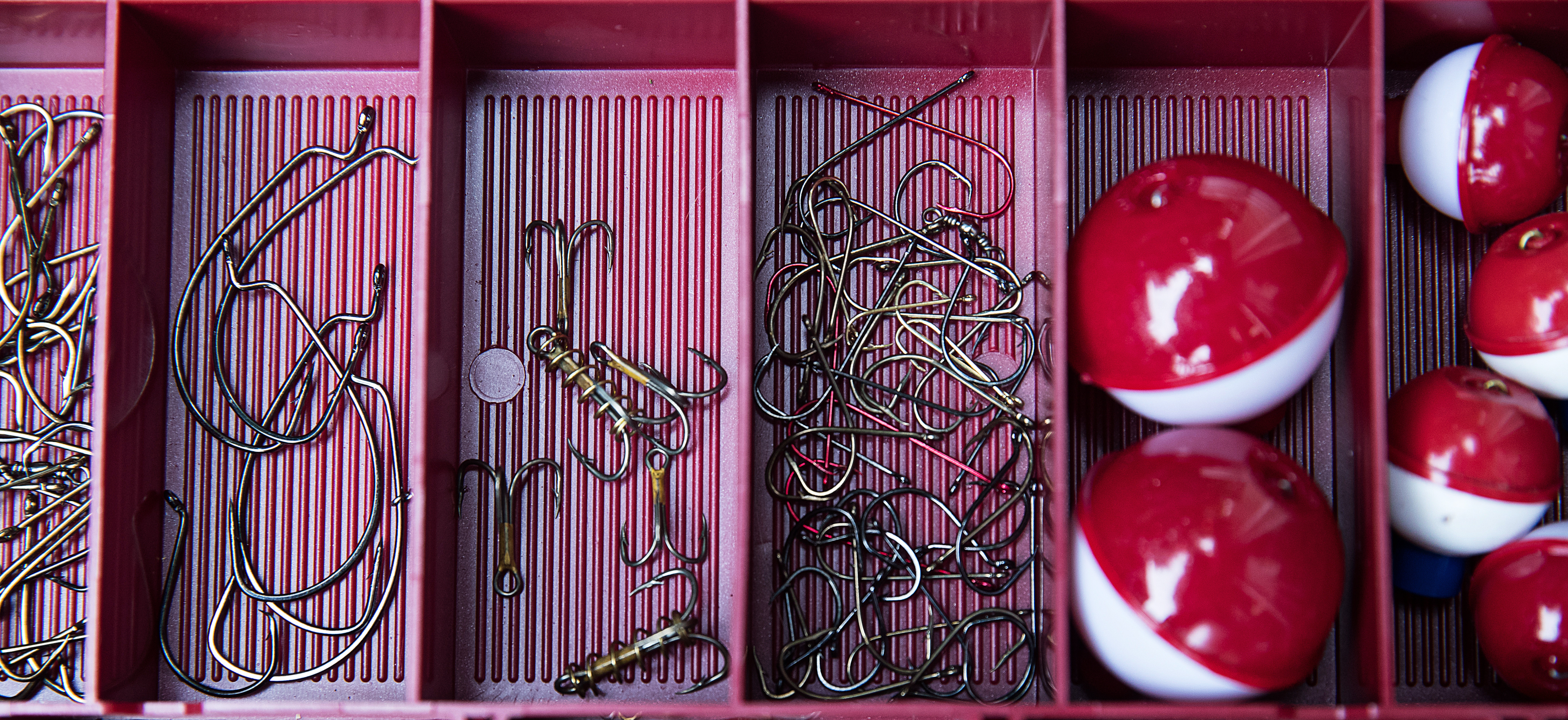 Hands holding various sizes of fishing hooks and bait